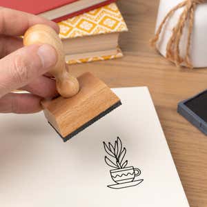 Hand pressing the Teacup Houseplant Craft Stamp onto cardstock beside a black ink pad
