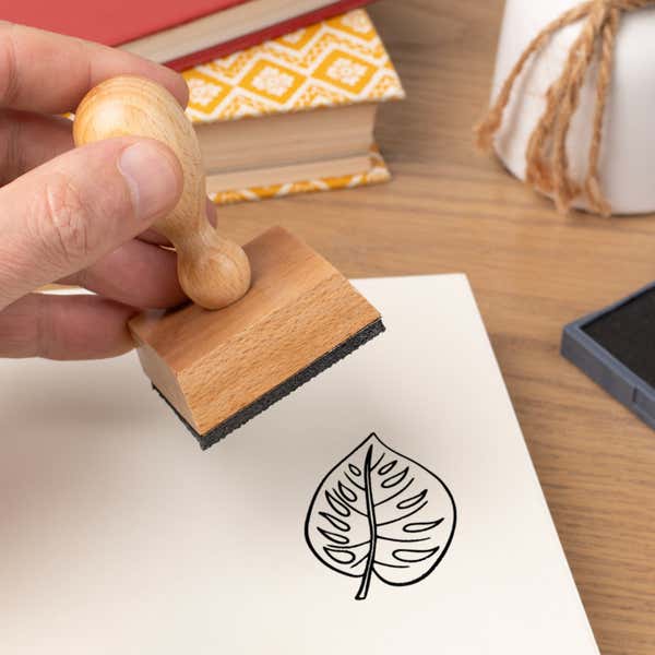 Hand pressing the Heart-Shaped Tropical Leaf Craft Stamp onto cardstock beside a black ink pad