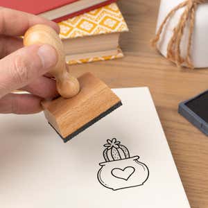Hand pressing the Heart Pot Cactus Craft Stamp onto cardstock beside a black ink pad