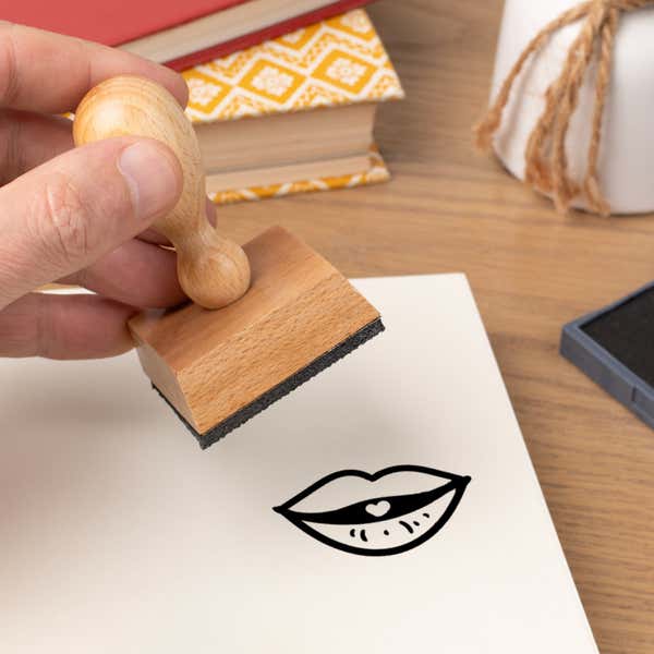 Hand pressing the Puckered Kissing Lips Craft Stamp onto cardstock beside a black ink pad