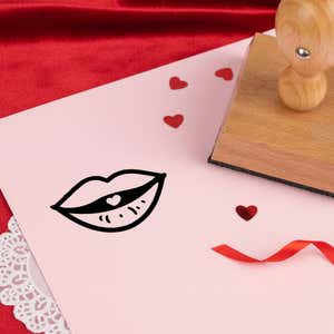 puckered kissing lips stamped in black on pink cardstock with red heart confetti, ribbon, a lace doily and the stamp