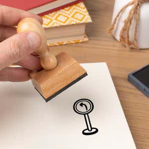 Hand pressing the Left Turn Sign Craft Stamp onto cardstock beside a black ink pad