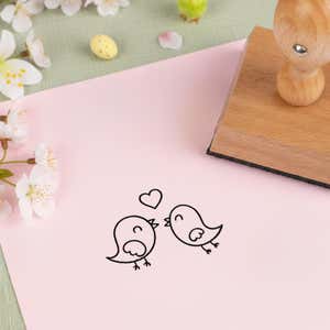 chirpy love birds stamped in black on pink cardstock beside white blossoms, a speckled candy egg and the wooden stamp