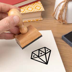 Hand pressing the Precious Love Diamond Craft Stamp onto cardstock beside a black ink pad