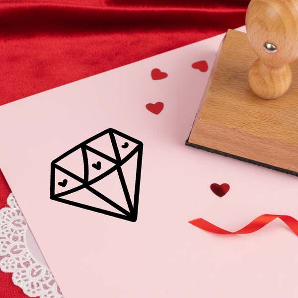precious love diamond stamped in black on pink cardstock with red heart confetti, ribbon, a lace doily and the stamp