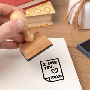 Hand pressing the Secret Love Note Craft Stamp onto cardstock beside a black ink pad