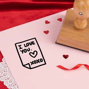 secret love note stamped in black on pink cardstock with red heart confetti, ribbon, a lace doily and the stamp