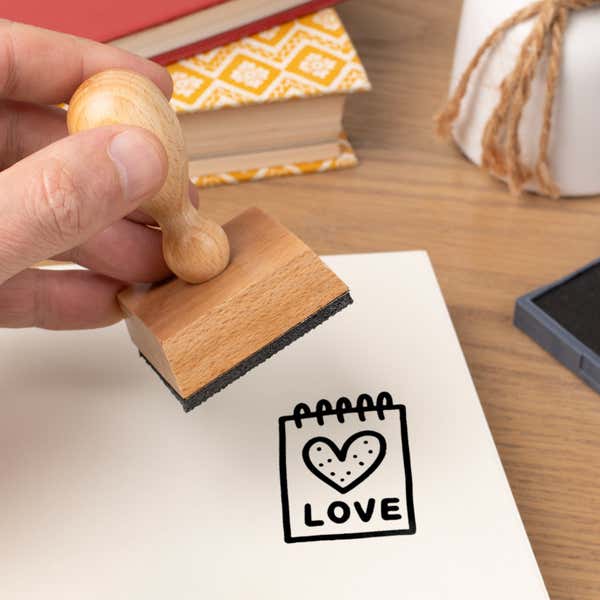 Hand pressing the Sweet Love Notepad Craft Stamp onto cardstock beside a black ink pad