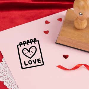 sweet love notepad stamped in black on pink cardstock with red heart confetti, ribbon, a lace doily and the stamp