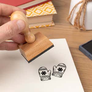 Hand pressing the Cozy Mittens Craft Stamp onto cardstock beside a black ink pad