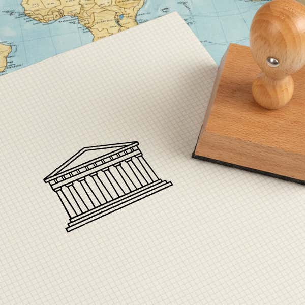 Parthenon stamped in black on cream graph paper laid over a world map, with the wooden stamp nearby