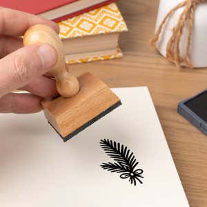 Hand pressing the Woodland Pine Branch Craft Stamp onto cardstock beside a black ink pad