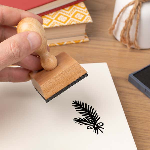 Hand pressing the Woodland Pine Branch Craft Stamp onto cardstock beside a black ink pad