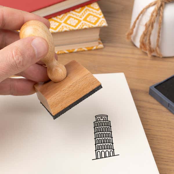 Hand pressing the Leaning Tower of Pisa Craft Stamp onto cardstock beside a black ink pad
