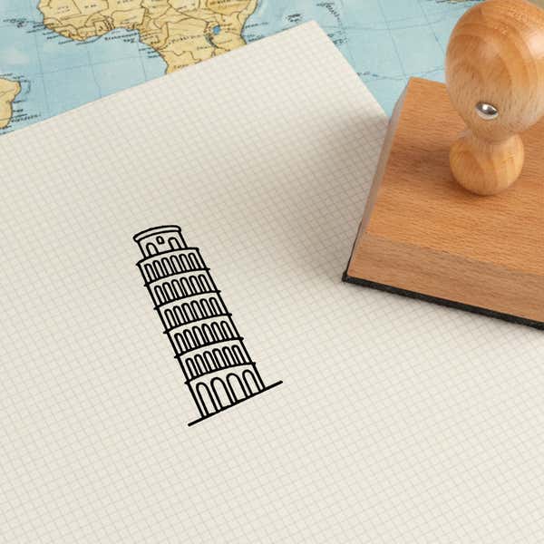 Leaning Tower of Pisa stamped in black on cream graph paper laid over a world map, with the wooden stamp nearby