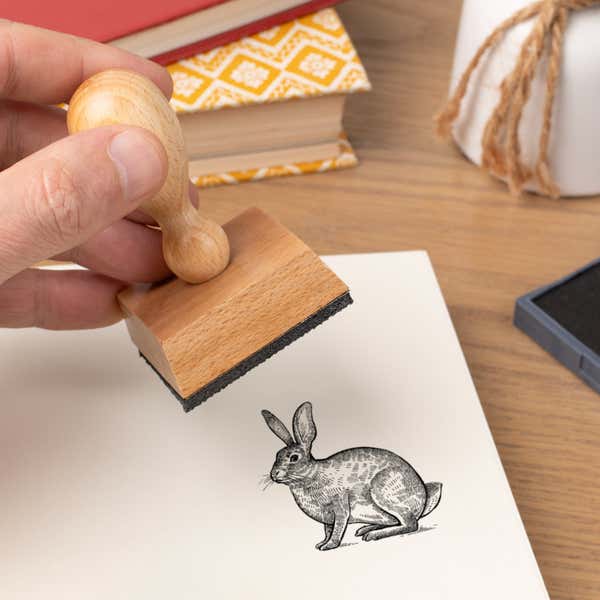 Hand pressing the Woodland Rabbit Craft Stamp onto cardstock beside a black ink pad