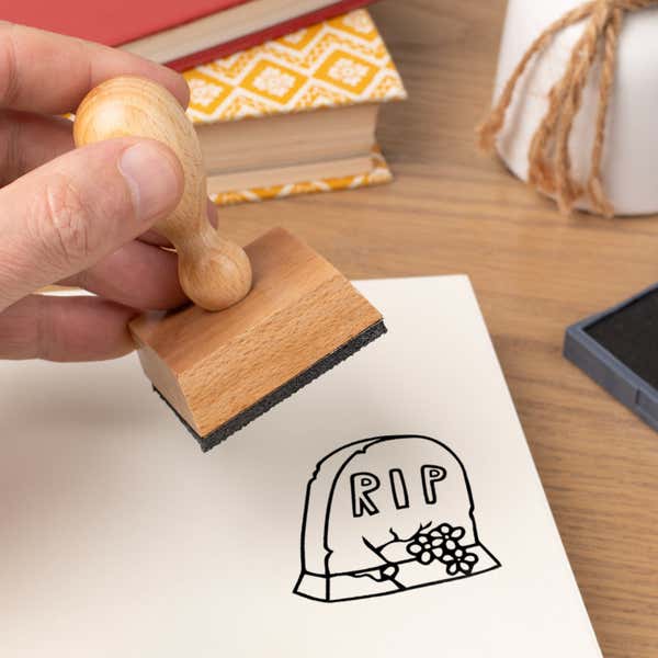 Hand pressing the Graveyard RIP Tombstone Craft Stamp onto cardstock beside a black ink pad