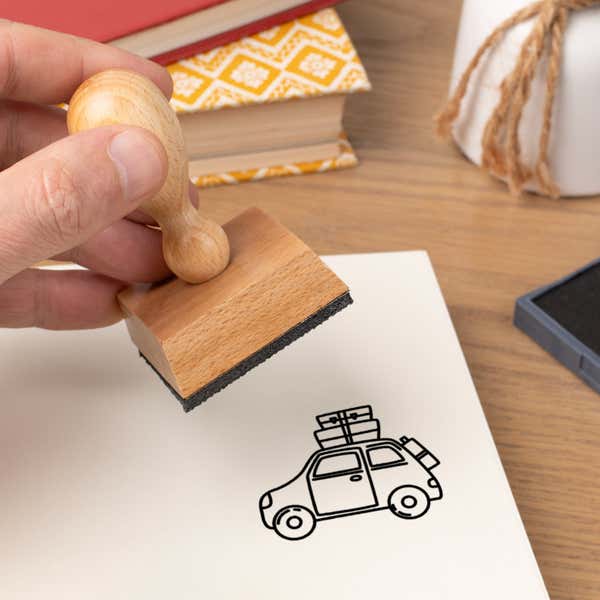 Hand pressing the Road Trip Car Craft Stamp onto cardstock beside a black ink pad