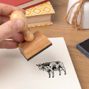Hand pressing the Sketched Cow Craft Stamp onto cardstock beside a black ink pad