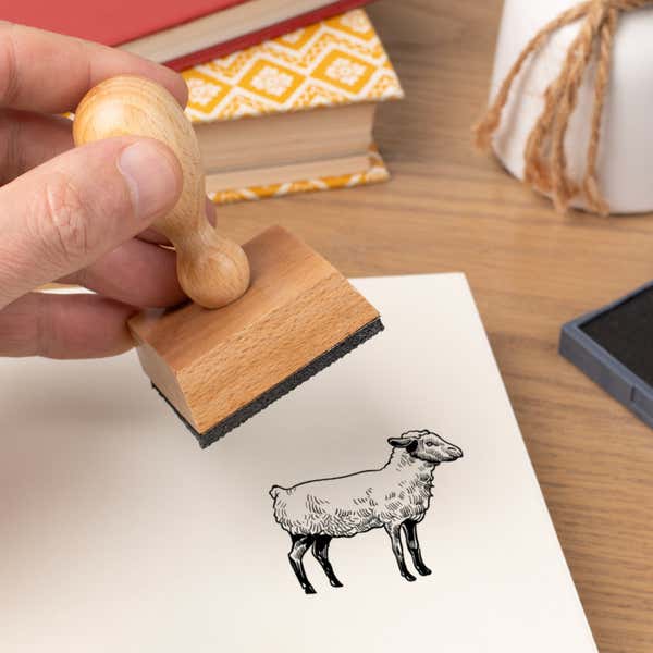 Hand pressing the Sketched Sheep Craft Stamp onto cardstock beside a black ink pad