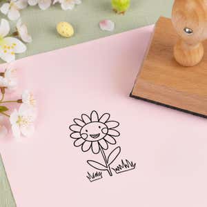 happy smiling daisy stamped in black on pink cardstock beside white blossoms, a speckled candy egg and the wooden stamp