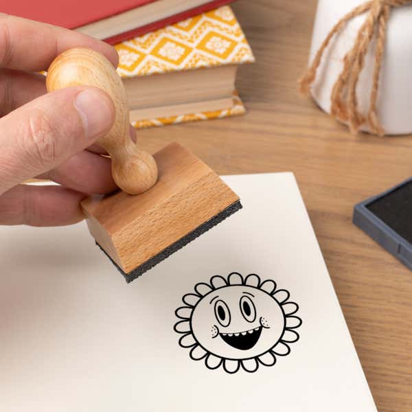 Hand pressing the Grinning Retro Flower Craft Stamp onto cardstock beside a black ink pad