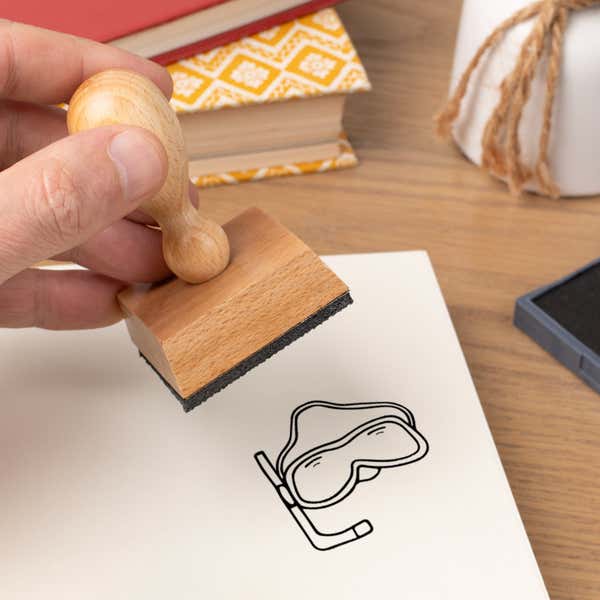 Hand pressing the Snorkel Mask Craft Stamp onto cardstock beside a black ink pad