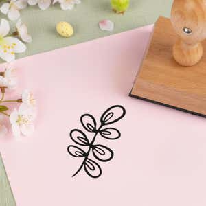 dainty spring sprig stamped in black on pink cardstock beside white blossoms, a speckled candy egg and the wooden stamp