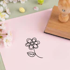 blooming spring flower stamped in black on pink cardstock beside white blossoms, a speckled candy egg and the wooden stamp