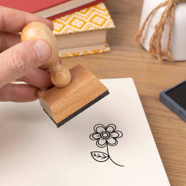 Hand pressing the Blooming Spring Flower Craft Stamp onto cardstock beside a black ink pad