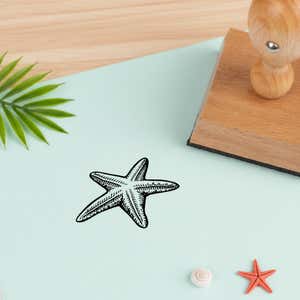 seashore starfish stamped in black on pale aqua cardstock beside a palm frond, a white seashell and a coral starfish