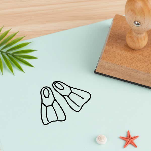 swim fins stamped in black on pale aqua cardstock beside a palm frond, a white seashell and a coral starfish
