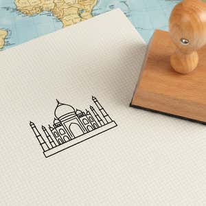 Taj Mahal stamped in black on cream graph paper laid over a world map, with the wooden stamp nearby
