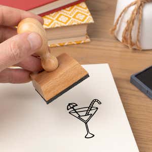 Hand pressing the Tropical Drink Craft Stamp onto cardstock beside a black ink pad
