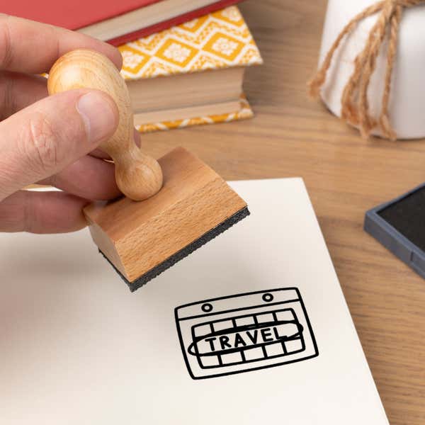 Hand pressing the Travel Graphic Craft Stamp onto cardstock beside a black ink pad