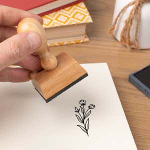Hand pressing the Dainty Bud Stems Craft Stamp onto cardstock beside a black ink pad