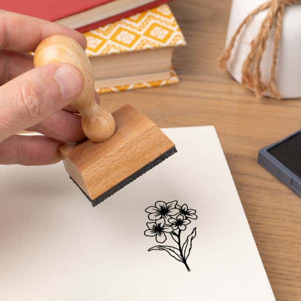 Hand pressing the Clustered Blossom Spray Craft Stamp onto cardstock beside a black ink pad