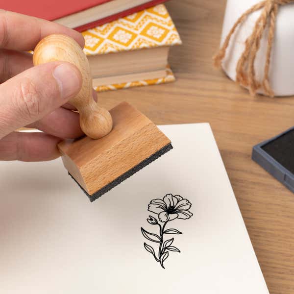 Hand pressing the Ruffled Bloom and Bud Craft Stamp onto cardstock beside a black ink pad