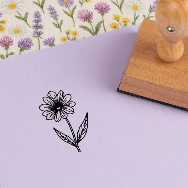 Fine-line daisy stem stamped in black on lilac cardstock on wildflower-print fabric