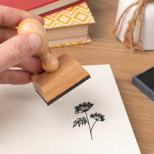 Hand pressing the Lacy Umbel Wildflower Craft Stamp onto cardstock beside a black ink pad