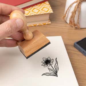 Hand pressing the Six-Petal Meadow Flower Craft Stamp onto cardstock beside a black ink pad