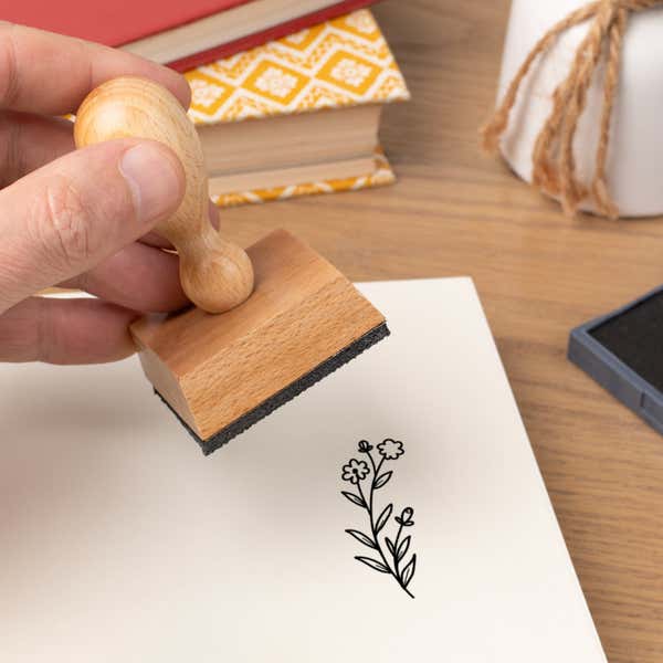 Hand pressing the Little Blossom Sprig Craft Stamp onto cardstock beside a black ink pad