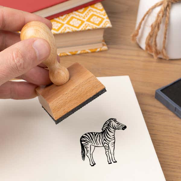 Hand pressing the Safari Zebra Craft Stamp onto cardstock beside a black ink pad
