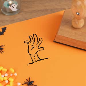 undead zombie hand stamped in black on orange cardstock next to candy corn, a plastic spider and a wooden stamp