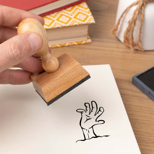Hand pressing the Undead Zombie Hand Craft Stamp onto cardstock beside a black ink pad