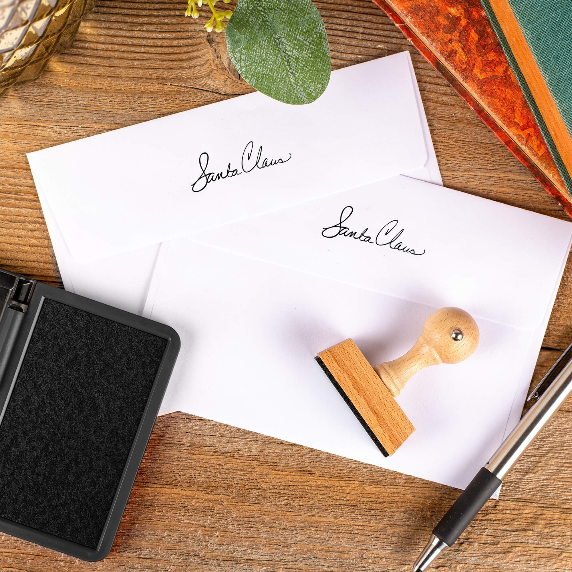 Santa Claus signature European hand stamp printed on the back flaps of two white envelopes with ink pad and stamp on wooden surface.