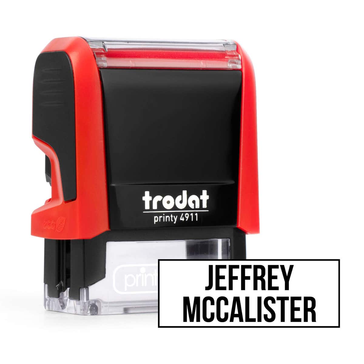 Red Trodat 4911 self-inking clothing stamp angled beside a boxed name imprint in the Bold font, a heavy condensed all-caps print.