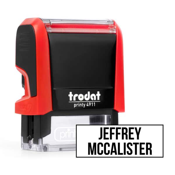 Red Trodat 4911 self-inking clothing stamp angled beside a boxed name imprint in the Bold font, a heavy condensed all-caps print.