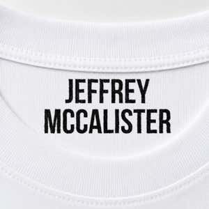 Close-up of a name stamped inside a white t-shirt collar in the Bold font, a heavy condensed all-caps print.