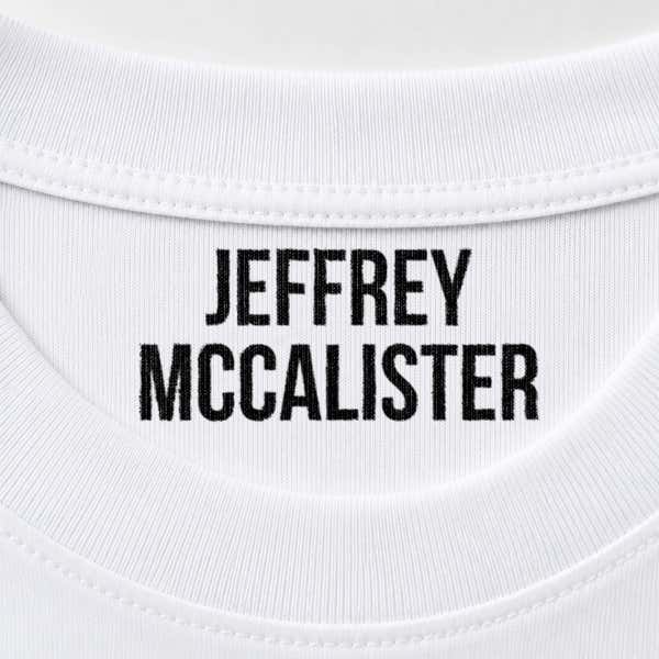 Close-up of a name stamped inside a white t-shirt collar in the Bold font, a heavy condensed all-caps print.